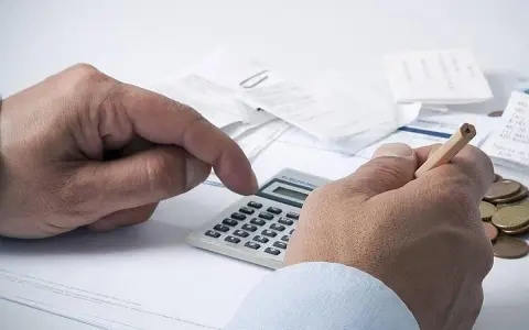 Manos calculando con calculadora y lápiz, rodeado de recibos y monedas. ¿Qué significa grupo de cotización 10?