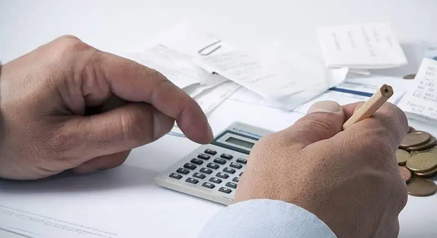 Manos calculando con calculadora y lápiz, rodeado de recibos y monedas. ¿Qué significa grupo de cotización 10?