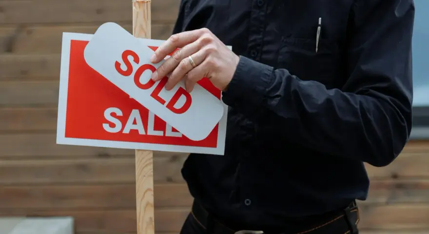 Hombre coloca cartel de "Vendido" sobre uno de "En Venta". Una venta rápida, quizás por debajo del valor de referencia.