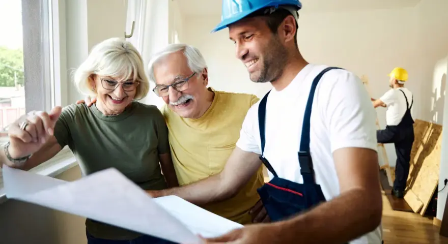 Pareja mayor sonríe mientras revisa planos con un constructor. Posibles bonificaciones mayores 65 años para su proyecto.