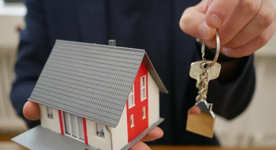 Mano ofrece maqueta de casa y llaves, símbolo de propiedad y seguridad ante la ley antiokupas.