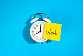 Reloj despertador blanco con nota amarilla que dice "Work", recordando la importancia de la jornada laboral.