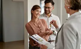 Pareja feliz recibe las llaves de su nuevo hogar, con un agente inmobiliario mostrando las escrituras de una casa.