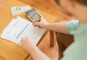 Persona revisa documentos y billetes, calculando cómo hacer un recibo de pago.