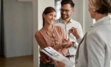 Pareja feliz recibe las llaves de su nuevo hogar, con un agente inmobiliario mostrando las escrituras de una casa.