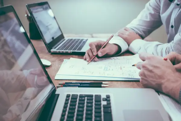 Dos personas revisan documentos y trabajan en laptops. Un modelo 200 cuando se presenta, con gráficos y notas.